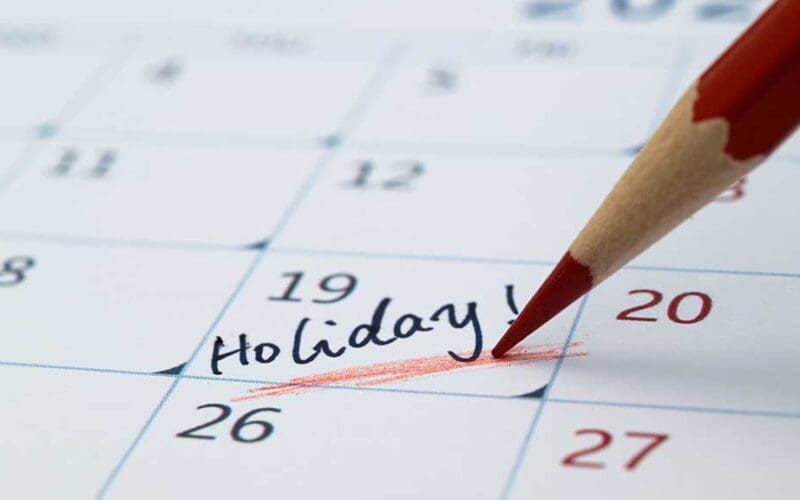Desk calendar and passport beside a laptop as a traveller plans annual leave in 2027 around bank holidays