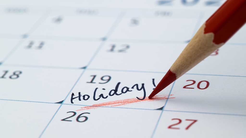 Desk calendar and passport beside a laptop as a traveller plans annual leave in 2027 around bank holidays